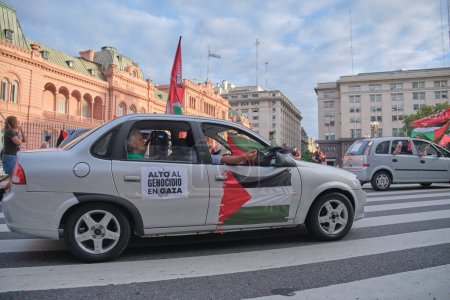 Foto de Buenos Aires, Argentina, 16 de febrero de 2024: Caravana de protesta en Plaza de Mayo, en solidaridad con Palestina, contra el ataque de Israel. Coche con banderas palestinas y afiche: Alto al genocidio en Gaza! - Imagen libre de derechos