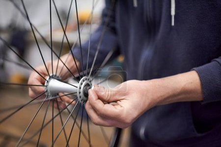 Personne méconnaissable qui assemble un essieu de roue de vélo après l'avoir démonté pour le nettoyage et le graissage dans le cadre d'un service d'entretien. De vraies personnes au travail.