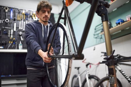 Hispanic man evaluating the alignment of the rear wheel of a bicycle he is servicing in his workshop. Real people at work.