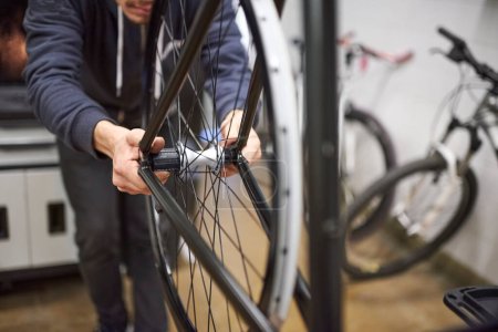 Technicien de vélo évaluant l'alignement de la roue arrière d'un vélo qu'il entretient dans son atelier. De vraies personnes au travail.