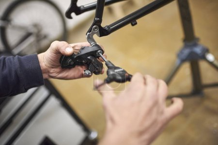 Homme méconnaissable assemblant le système de freinage d'un vélo dans le cadre du service d'entretien qu'il effectue dans son atelier. De vraies personnes au travail.