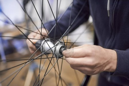 Photo for Unrecognizable man assembling a bike wheel axle after disassembling it for cleaning and greasing as part of a bicycle maintenance service. Real people at work. - Royalty Free Image