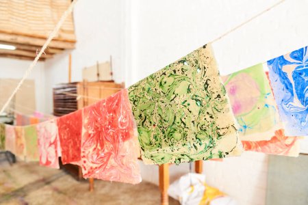 Bunte Blätter aus handgeschöpftem Papier, frisch gefärbt mit der Marmoriertechnik, die an Seilen zum Trocknen hängt.