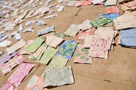 Colorful sheets of handmade paper freshly dyed with the marbling technique spread out on the ground, drying.