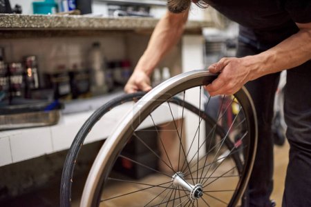 Ein hispanischer Fahrradmechaniker montiert in einer Werkstatt einen luftlosen Vollreifen an einem Rad. Selektive Fokuskomposition mit Kopierraum.