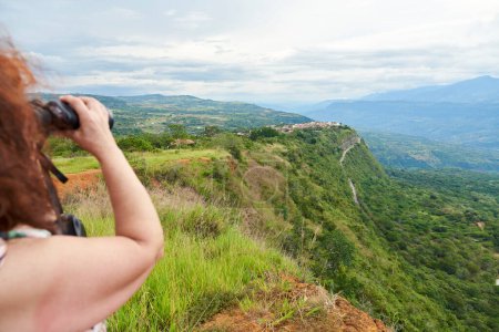 Eine unkenntliche Frau beobachtet Barichara, die schönste Stadt Kolumbiens, von einem Aussichtspunkt aus durch ein Fernglas.