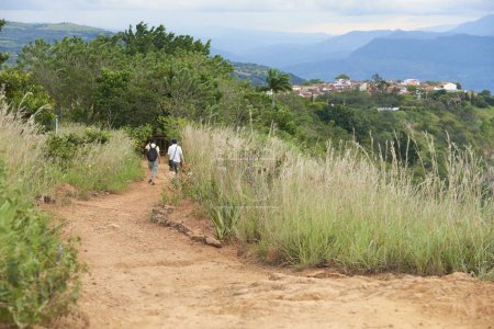 Paar unkenntlich gemachte Reisende, die von hinten auf einer unbefestigten Straße in einem natürlichen Touristengebiet in Richtung Barichara, der schönsten Stadt Kolumbiens, spazieren.