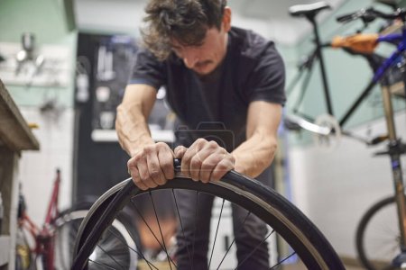 El técnico de bicicletas hispano monta un neumático sólido sin aire en una rueda de bicicleta en su taller de reparación. Composición de enfoque selectivo con espacio de copia.