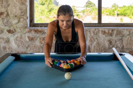 A focused woman prepares to break the rack of pool balls on a billiard table