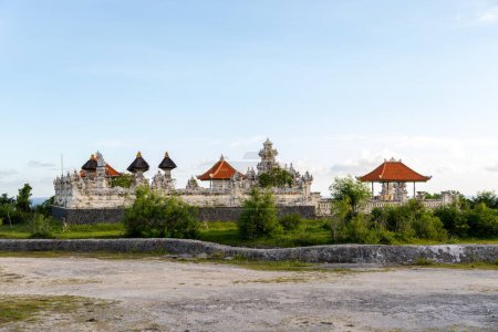 Traditional Balinese architecture with distinctive rooftops stands atop a limestone quarry, surrounded by greenery under a clear sky