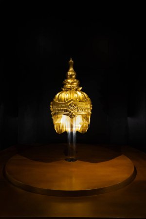A radiant golden helmet sculpture displayed against a dark background, symbolizing regal elegance and historical significance