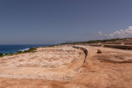 Humans permanently destroy unique natural landscapes with heavy machinery and excavation of cliffside terrain for business ventures in Bali. The cleared area overlooks the ocean, highlighting