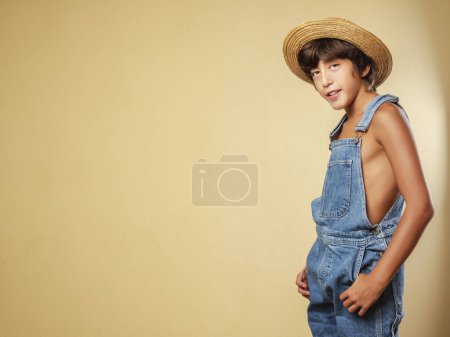 Photo for Farmer boy dressed in dungarees and a straw hat. Copy space. - Royalty Free Image
