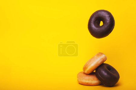 Horizontal photograph of sugar and chocolate doughnuts falling one on top of the other in a pile on a vibrant yellow background.