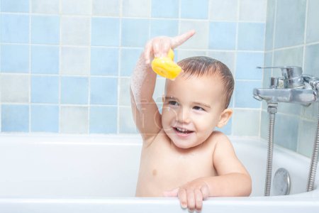 Little boy in the bathtub showing his rubber ducky to the camera