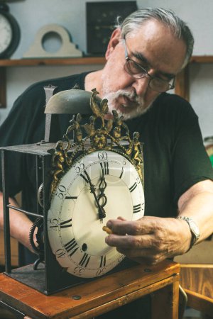 Téléchargez les photos : Vue de face d'un horloger réparant une grande horloge antique. Vous pouvez voir quelques-uns des engrenages et le passage du temps sur le cadran de l'horloge. - en image libre de droit