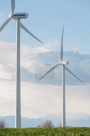 Deux éoliennes sont debout dans un champ avec un ciel nuageux en arrière-plan. Les turbines sont hautes et blanches, et ce sont les seules structures visibles dans l'image