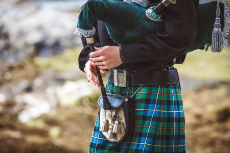 A man wearing a kilt and holding a pipe. The man is dressed in traditional Scottish clothing and is playing a pipe. Concept of cultural pride and heritage, as well as a connection to the past