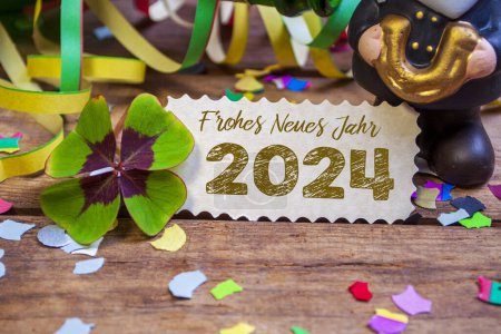 Holzhängeanhänger und Schiefer mit vierblättrigem Kleeblatt und Wunderkerzen mit den deutschen Worten für ein frohes neues Jahr - frohes neues Jahr 2024 auf verwittertem Holzgrund