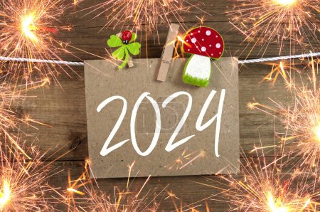 Holzhängeanhänger und Schiefer mit vierblättrigem Kleeblatt und Wunderkerzen mit den deutschen Worten für ein frohes neues Jahr - frohes neues Jahr 2024 auf verwittertem Holzgrund