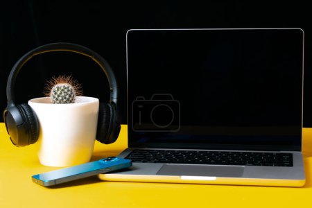 Téléchargez les photos : Table de bureau avec cactus, écouteurs, smartphone et ordinateur portable - en image libre de droit