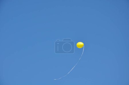 Photo for Single yellow balloon with long cord flown away against a bright blue sky - Royalty Free Image