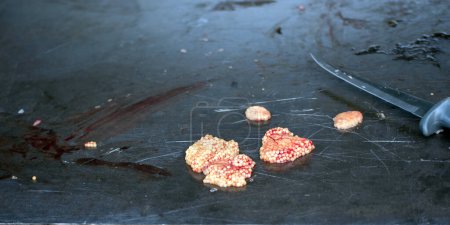 Small masses of yellow fish eggs with red veins sit on a black table after the fish have been cleaned for eating. A sharp defocused fillet knife also sits on the table.