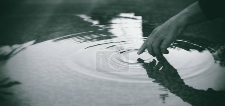 Photo for Detail of a hand touching lake water surface leaving ripples in concentric circles. People in nature. Unity, harmony and mindfulness concept. Monochrome panorama banner with copy space - Royalty Free Image