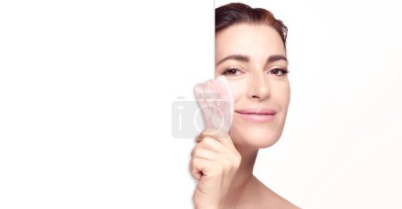 Photo for Beauty and skincare concept. Beautiful woman with gua sha tool. Middle aged female showing guasha for massage facial lifting. isolated on white background banner - Royalty Free Image