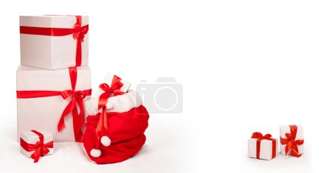 Téléchargez les photos : Carte de Noël avec le sac du Père Noël à côté d'autres cadeaux de Noël. Coffrets cadeaux enveloppés dans des boîtes blanches décorées de grands rubans rouges. Isolé sur fond blanc avec espace de copie central - en image libre de droit