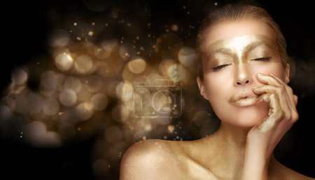 Téléchargez les photos : Concept de soins anti-âge à base d'or. Belle femme modèle avec traitement d'or posant avec les yeux fermés et une expression sereine sur fond bokeh or - en image libre de droit