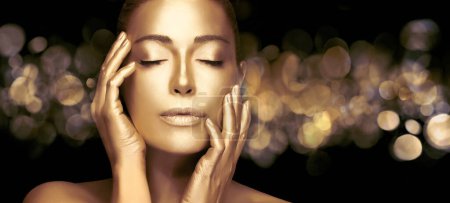 Gold based anti aging skin care concept. Beautiful model woman with gold on skin raising her hands gracefully to her face with eyes closed and a serene expression. Gold for mature skincare.
