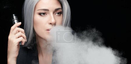 Vaping girl. Silver haired woman blowing a big smoke cloud. Female with an Electronic Cigarette isolated on black background with copy space