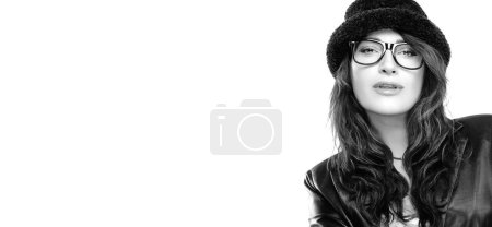 Téléchargez les photos : Ophthalmology and eye care. Stylish sensual woman in chic black outfit with hat and eyeglasses giving the camera a sultry look. Beauty monochrome portrait over white background with copy space - en image libre de droit