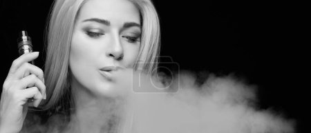 Foto de Monochrome vaping girl. Silver haired woman blowing a big smoke cloud. Female with an Electronic Cigarette isolated on black background with copy space - Imagen libre de derechos