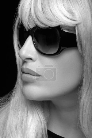 Foto de Monochrome fashion portrait of an attractive blonde woman with healthy long hair, wearing black sunglasses. Close-up portrait isolated on black background in vertical format - Imagen libre de derechos
