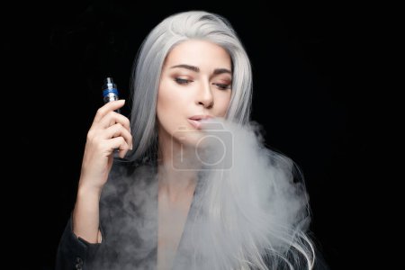 Photo for Sensual gray haired woman using electronic cigarette. Beauty model woman with a vaping device blowing a white cloud of smoke. Horizontal portrait isolated on black background with copy space - Royalty Free Image