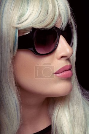Photo for Fashion portrait of an attractive blonde woman with healthy long hair, wearing black sunglasses. Close-up portrait isolated on black background in vertical format - Royalty Free Image
