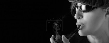 Téléchargez les photos : Gorgeous woman smoking pipe. Smoking lady with a vintage wooden pipe. Closeup monochrome studio portrait isolated on black with copy space - en image libre de droit
