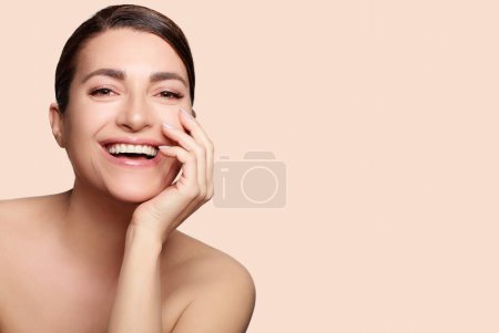 Concepto de belleza y cuidado de la piel. Mujer natural sonriente con maquillaje desnudo en una piel impecable. Retrato de estudio sobre fondo beige