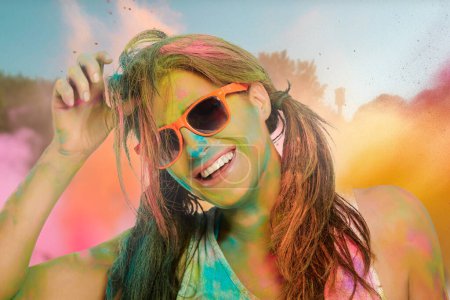 Foto de Mujer alegre y despreocupada cubierta de polvo de color arco iris celebrando el festival de colores. Mujer joven divirtiéndose con colorido polvo de holi al aire libre - Imagen libre de derechos