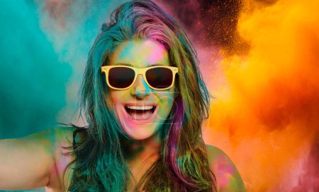 Foto de Mujer alegre y despreocupada cubierta de polvo de color arco iris celebrando el festival de colores. Mujer joven divirtiéndose con polvo de holi colorido. - Imagen libre de derechos