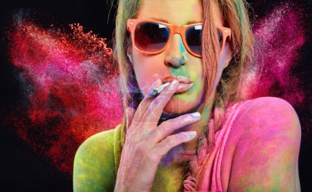 Photo for Beautiful woman covered in rainbow colored powder smoking a cigarette. Close-up portrait isolated on a black panorama background with copyspace - Royalty Free Image