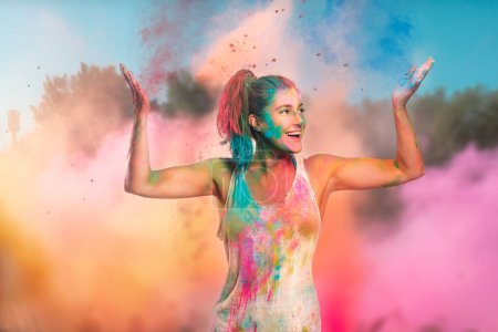 Photo for Carefree cheerful woman covered in rainbow colored powder celebrating the festival of colors. Young woman having fun with colorful holi powder - Royalty Free Image