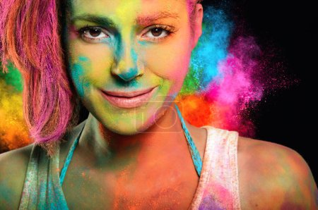Foto de Mujer joven con pinturas holi y una explosión de color arco iris en el fondo. - Imagen libre de derechos