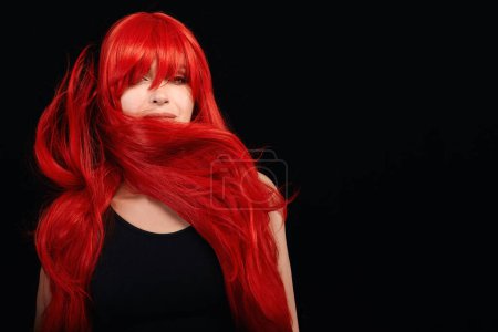 Photo for Dyed hair care and fashion concept. Fashion model girl with windswept long dyed red hair, isolated on black with copy space. - Royalty Free Image