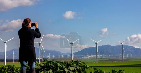 Foto de Una mujer fotografía un aerogenerador en un campo, un símbolo de la energía renovable. Con copyspace - Imagen libre de derechos