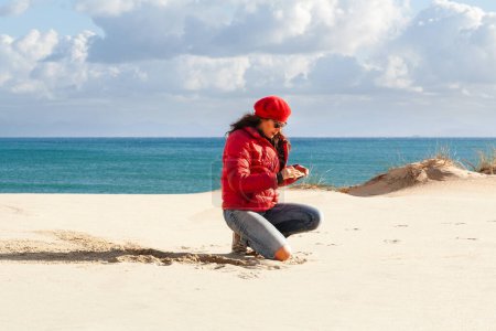 Téléchargez les photos : Femme Nomad numérique sur la plage, pleine longueur, Horizon sur l'eau, Utilisation Smartphone. Avec espace de copie. - en image libre de droit