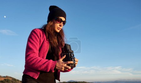 Téléchargez les photos : Une femme vêtue de rouge et portant des lunettes de soleil est à l'extérieur, prenant des photos sous un ciel clair. Elle est entourée d'un grand espace de copie qui permet à diverses fins éditoriales ou de conception. - en image libre de droit
