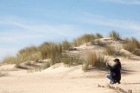 Foto de Mujer en una duna de arena con smartphone en un vasto paisaje natural. Copiar espacio. - Imagen libre de derechos